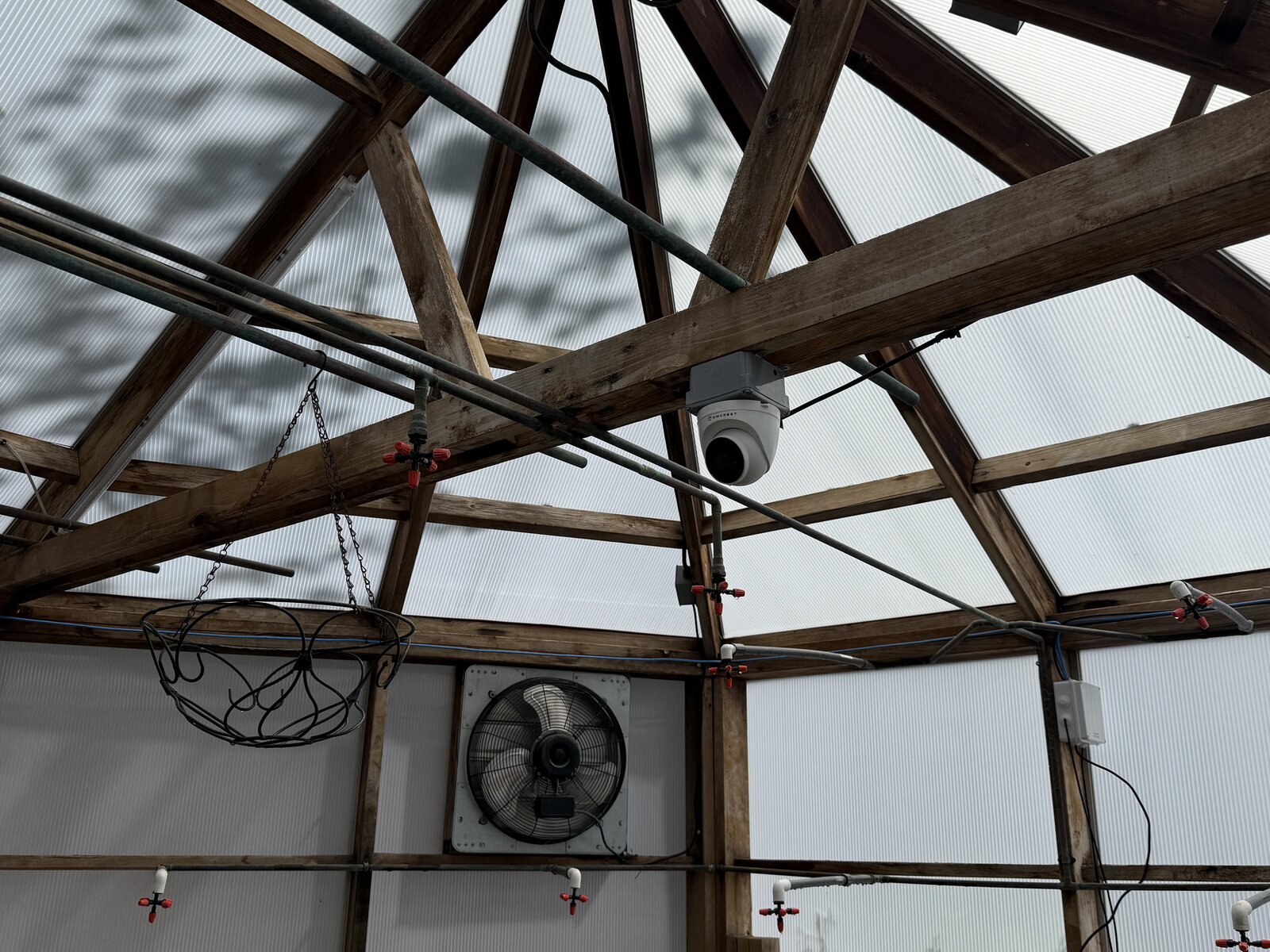 Security camera at the roof apex and exhaust fan on the south gable, part of the integrated monitoring and ventilation system